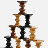 Seven Eames Turned Stools, Shape D by Herman Miller are stacked in a pyramid, showcasing their solid walnut and lighter finishes against a plain white background.