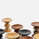 A cluster of HERMAN MILLER Eames Turned Stool, Shape D in solid walnut and other wood finishes—light, medium, dark brown, and black—stands sculpturally against a plain white background.