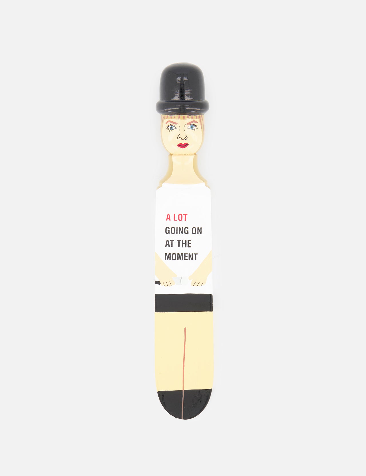 The WEDGIE "Swifty" (Going On Outfit) Wood Door Stopper features a hand-painted figure in a black bowler hat, white shirt with "A LOT GOING ON AT THE MOMENT," yellow pants, and black shoes against a plain white background.