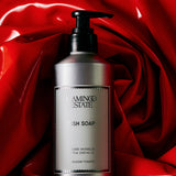A silver pump bottle of FLAMINGO ESTATE Heirloom Tomato Dish Soap rests on shiny, crumpled red fabric, suggesting a tomato leaf scent and made with biodegradable cleansers for an eco-friendly clean.