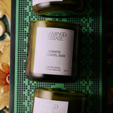The FLAMINGO ESTATE Three Sisters Candle Set, featuring Tuscan Rosemary, Adriatic Muscatel Sage, and Heirloom Tomato candles, sits on a green grid-patterned tray—an elegant housewarming gift for any home.