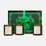 Three green glass FLAMINGO ESTATE Three Sisters candles with white labels sit in front of a black and green heart-patterned box tied with a bright green ribbon—the perfect gift set for a housewarming.