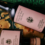 The Tablemates Boxed Oil & Vinegar Gift Set by FLAMINGO ESTATE features two bottles with light pink labels and black text on a decorative surface. Finished with a green ribbon, this elegant set includes Heritage Olive Oil and Balsamic Vinegar.