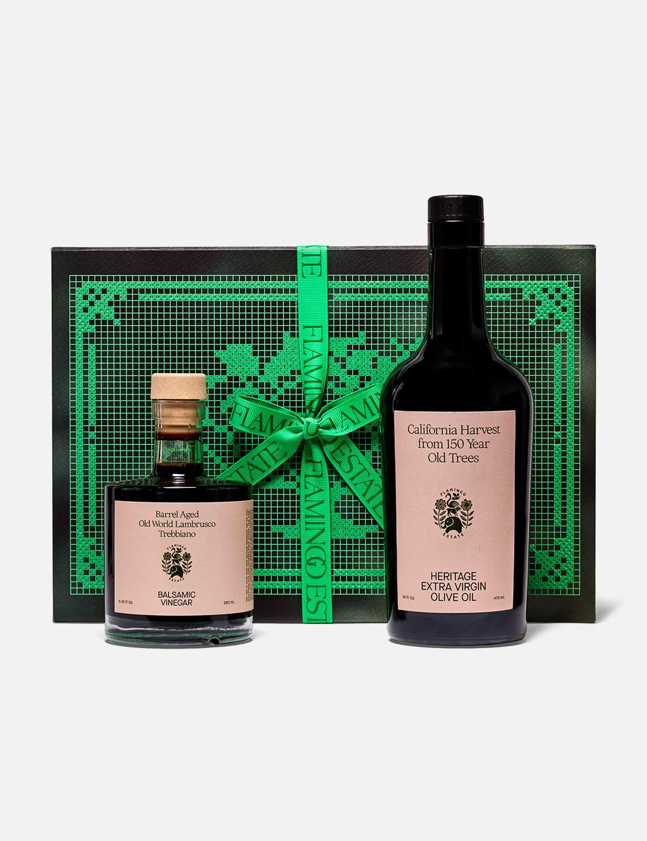 The Tablemates Boxed Oil & Vinegar Gift Set by FLAMINGO ESTATE features two Heritage Olive Oil bottles with light pink labels, presented before a black and green box tied with a green ribbon.