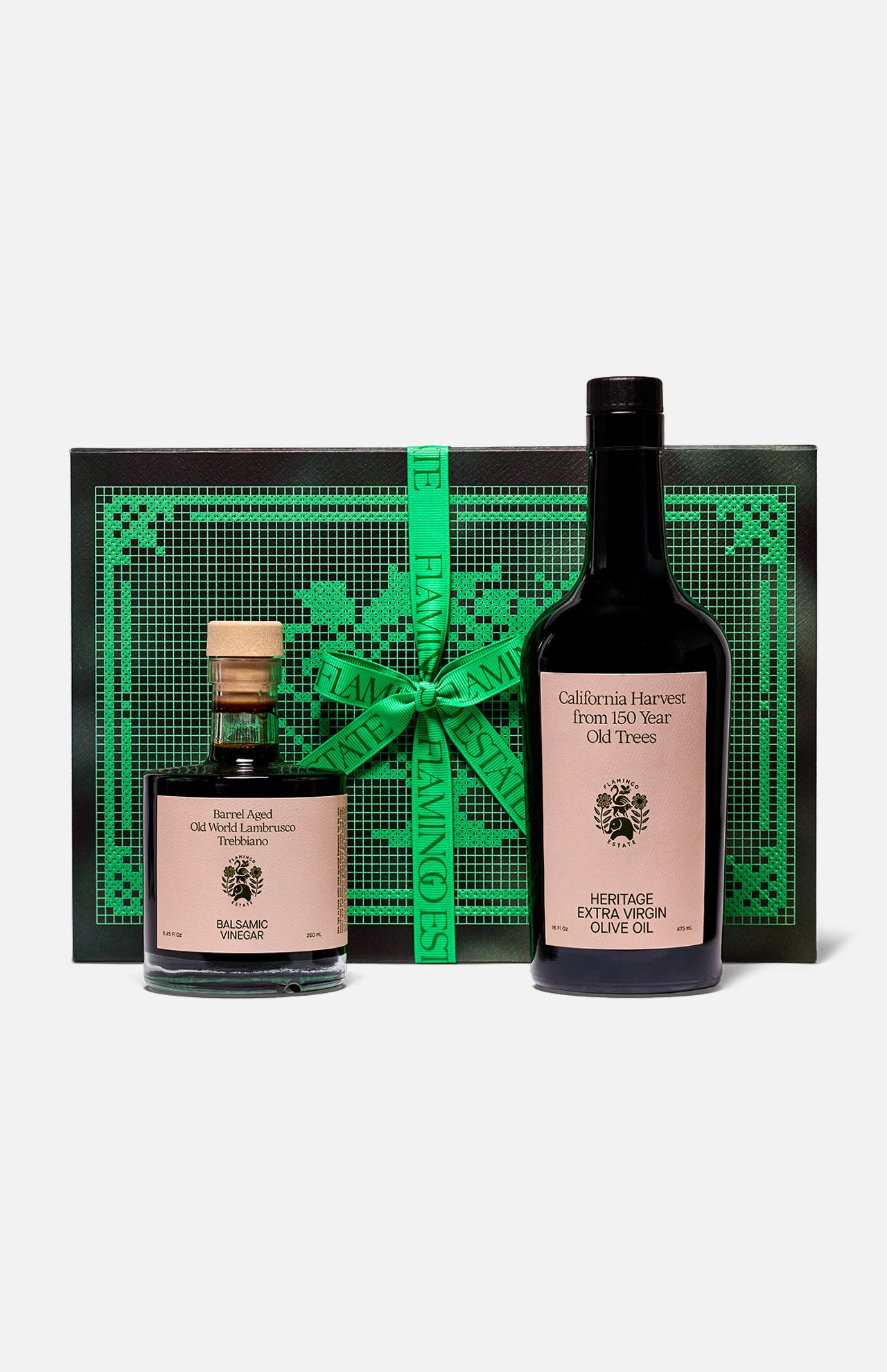 The Tablemates Boxed Oil & Vinegar Gift Set by FLAMINGO ESTATE features two Heritage Olive Oil bottles with light pink labels, presented before a black and green box tied with a green ribbon.