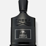 A black bottle of CREED Absolu Aventus 100 ml Fragrance with a silver label, displayed against a light gray background, embodies the essence of the iconic scent with its signature citrus notes.