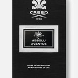 Sleek black box of CREED’s Absolu Aventus 100 ml Fragrance, highlighted by a striking white crest, "CREED 1760" text, and a silver-bordered label—with details including "100 ML" and "House Established 1760" at the bottom—an elegant presentation for this legendary scent celebrated for its vibrant pineapple patchouli notes and refined citrus aroma.
