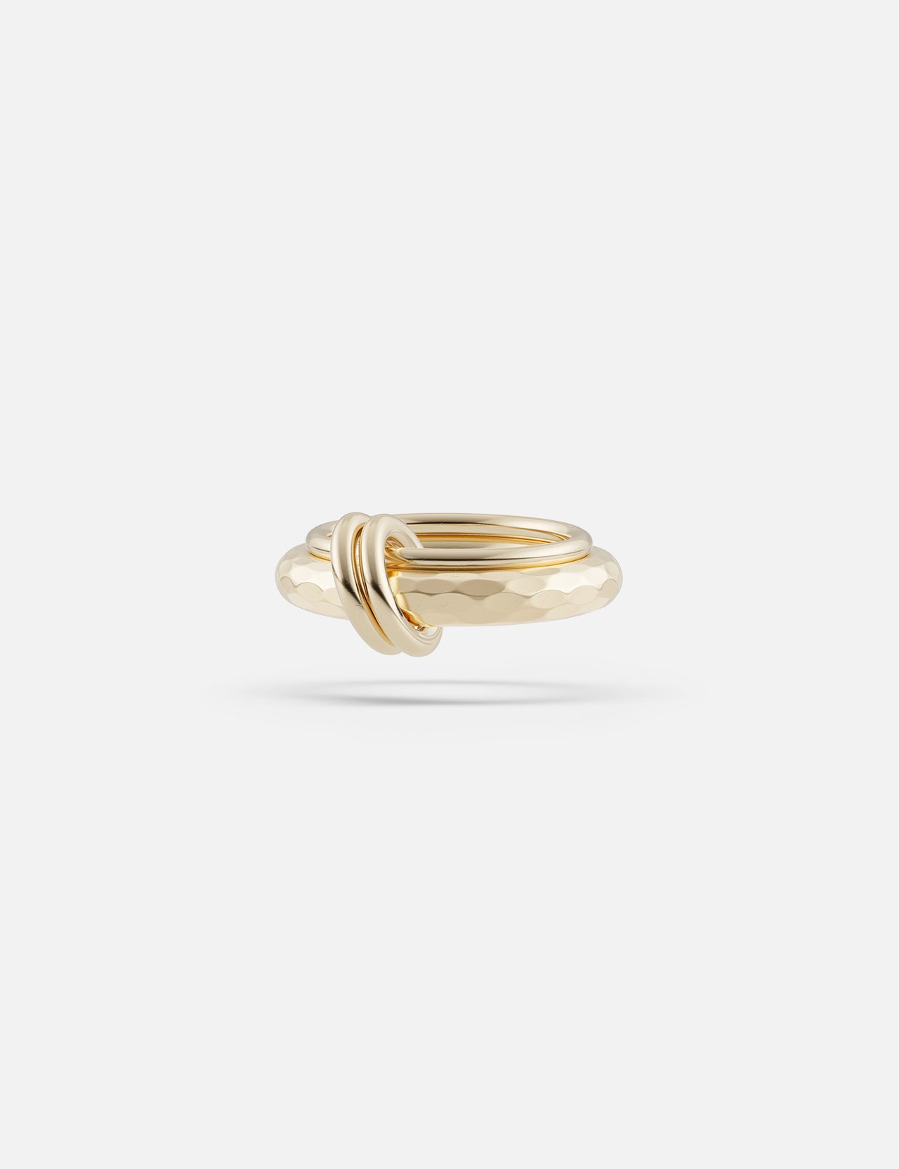 The Agon Vulcan Ring by SPINELLI KILCOLLIN features polished yellow gold with a hammered texture and a small knot accent on the band, inspired by modular jewelry and shown against a plain white background.