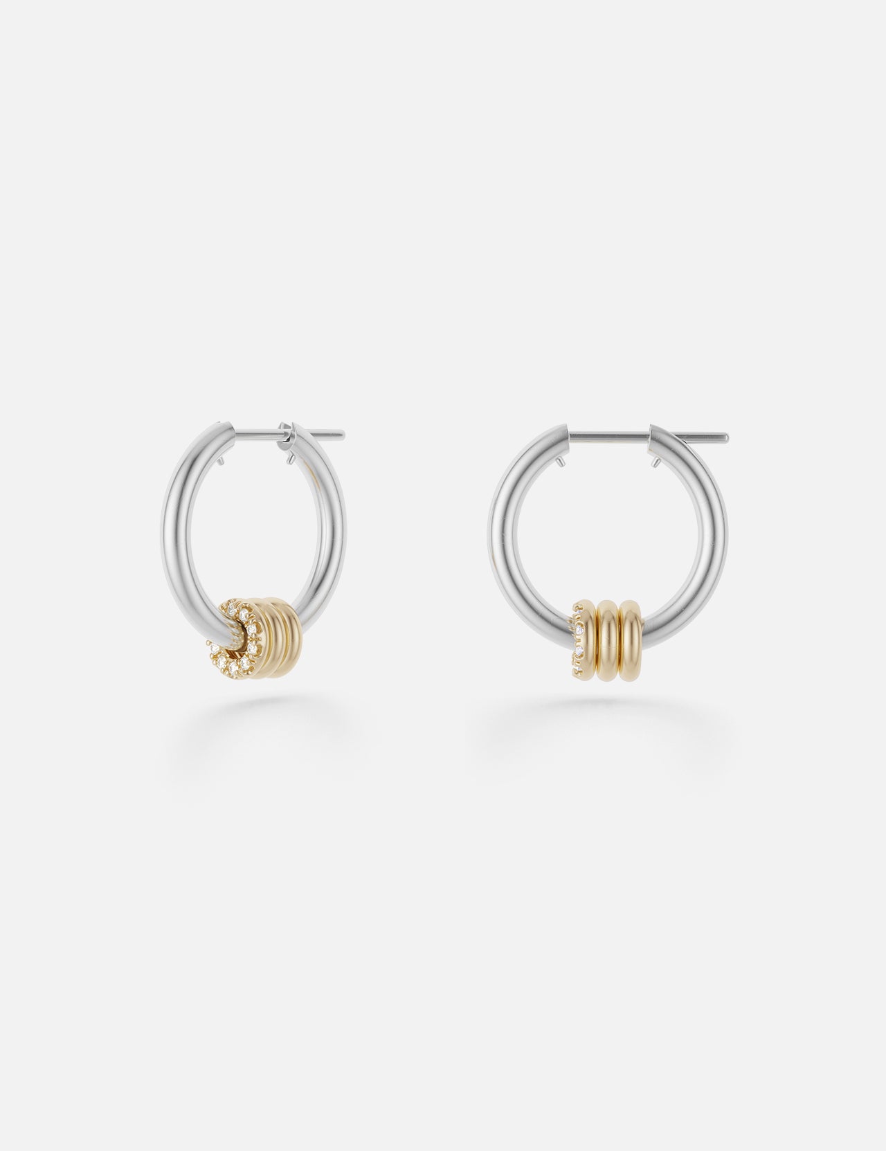 The Ara Deux Diamond Detail Earrings by SPINELLI KILCOLLIN are small sterling silver hoops featuring three gold rings as accents, shown on a plain white background.