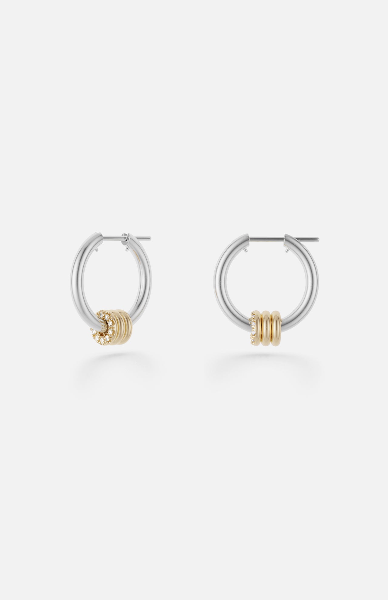 The Ara Deux Diamond Detail Earrings by SPINELLI KILCOLLIN are small sterling silver hoops featuring three gold rings as accents, shown on a plain white background.