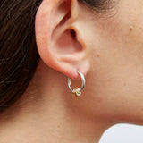 Close-up of a person's ear wearing SPINELLI KILCOLLIN's Ara Deux Diamond Detail Earrings. The sterling silver hoops with gold accents stand out against their straight brown hair and light skin, highlighting the elegant design.