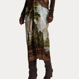 A person wearing the RALPH LAUREN COLLECTION Scenic Silk Twill Pencil Skirt—featuring a scenic landscape print with leopard print borders—paired with brown heeled boots and a dark long-sleeve top.