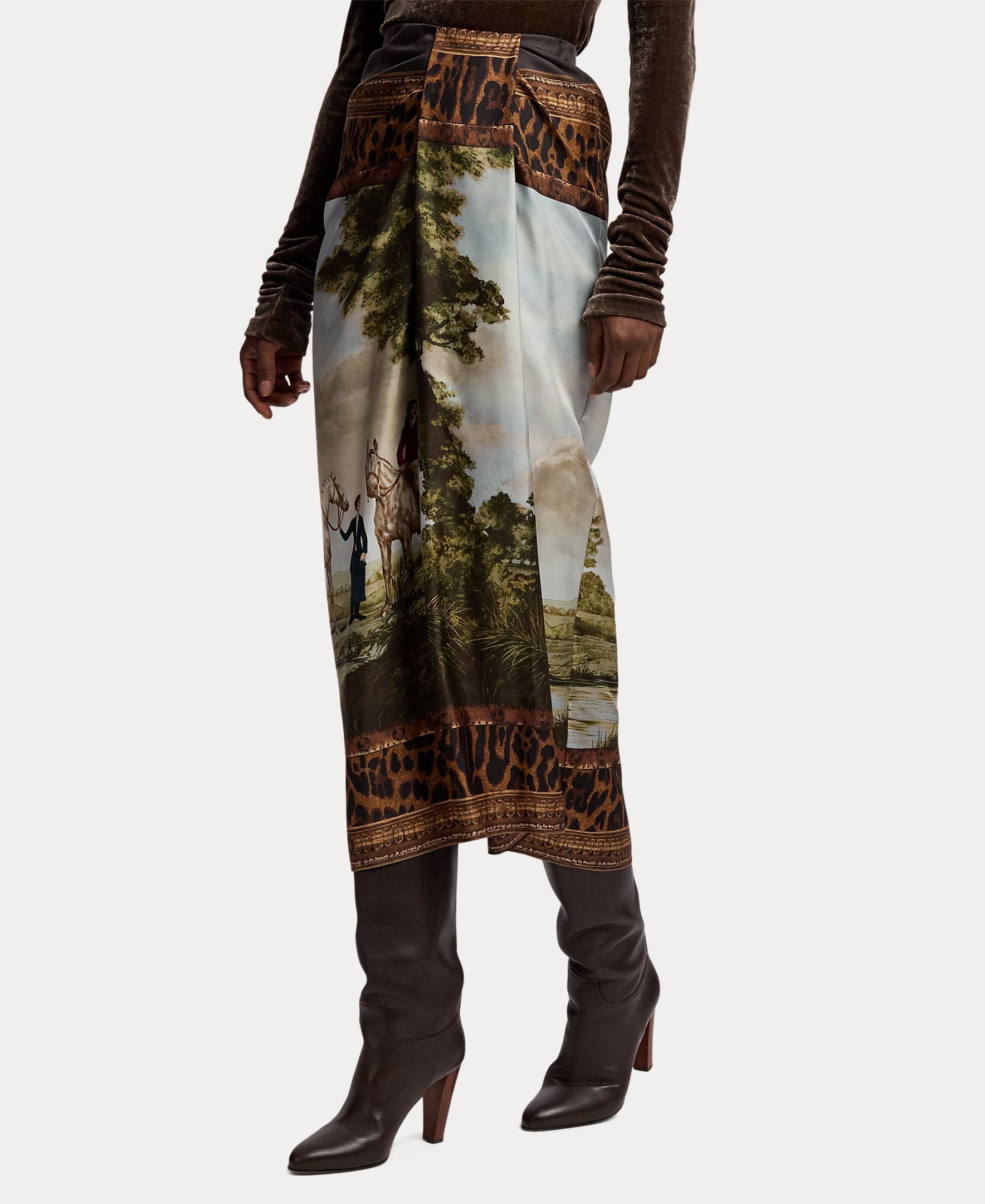 A person wearing the RALPH LAUREN COLLECTION Scenic Silk Twill Pencil Skirt—featuring a scenic landscape print with leopard print borders—paired with brown heeled boots and a dark long-sleeve top.