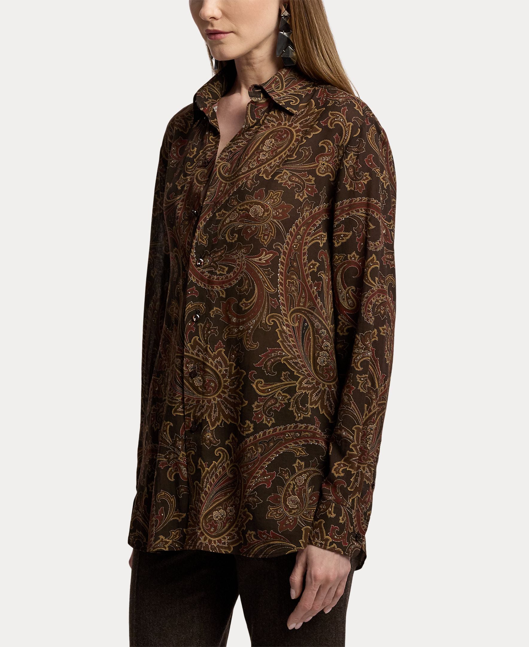 A person wearing the Paisley Collared Long Sleeve Blouse by RALPH LAUREN COLLECTION, featuring a relaxed fit and elegant brown and gold paisley print, paired with dark pants. The photo is cropped at the knees and does not reveal the full face—making it perfect inspiration for your fall wardrobe.