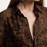 A woman wearing a RALPH LAUREN COLLECTION Paisley Collared Long Sleeve Blouse in a dark brown, long-sleeve button-down style with a multicolored paisley print and large geometric silver earrings.