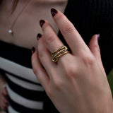 A close-up of a woman’s hand wearing the SPINELLI KILCOLLIN Sonny Pavé Band Ring in yellow gold, featuring a unique modular design, paired with dark red nail polish and a gold bracelet. She is dressed in a black and white striped top and a black sweater.