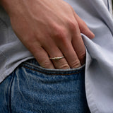 A close-up of a hand wearing the SPINELLI KILCOLLIN Sirius 3 Annulets Ring—a unisex gold ring with three beads—resting on the edge of a blue jean pocket. The person is also wearing a light gray shirt.
