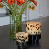 An ONNO Art Brigitte M Zanzibar Candle sits beside a green glass vase with orange and yellow flowers on a gray countertop, set against the backdrop of a modern, minimal kitchen.