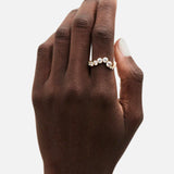 A hand with a natural nude manicure showcases the SOPHIE BILLE BRAHE Ensamble Ocean gold statement ring, featuring assorted round clear gemstones, photographed against a white background.