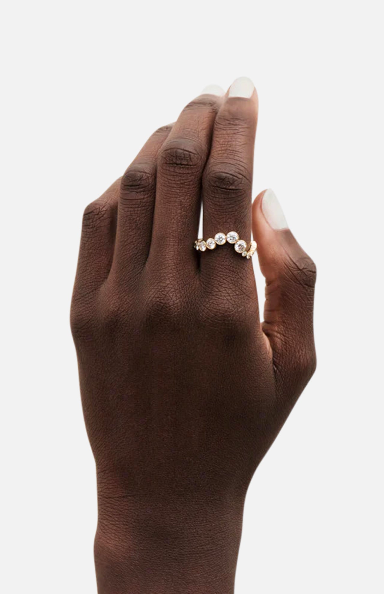 A hand with a natural nude manicure showcases the SOPHIE BILLE BRAHE Ensamble Ocean gold statement ring, featuring assorted round clear gemstones, photographed against a white background.