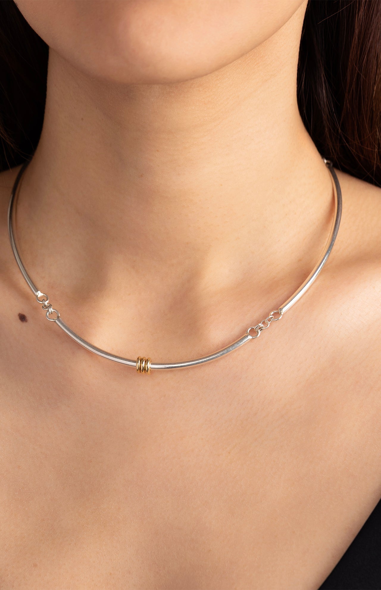 Close-up of a woman’s neck wearing the sleek SPINELLI KILCOLLIN Hello Tria Silver Necklace, featuring a small gold accent at the center, paired with a black top.