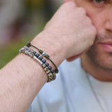 A close-up of a man's arm shows three bracelets: TATEOSSIAN's Classic Discs Dalmatian Jasper Bracelet, a sterling silver and black beaded bracelet, and a green string charm bracelet—stylishly made in London.