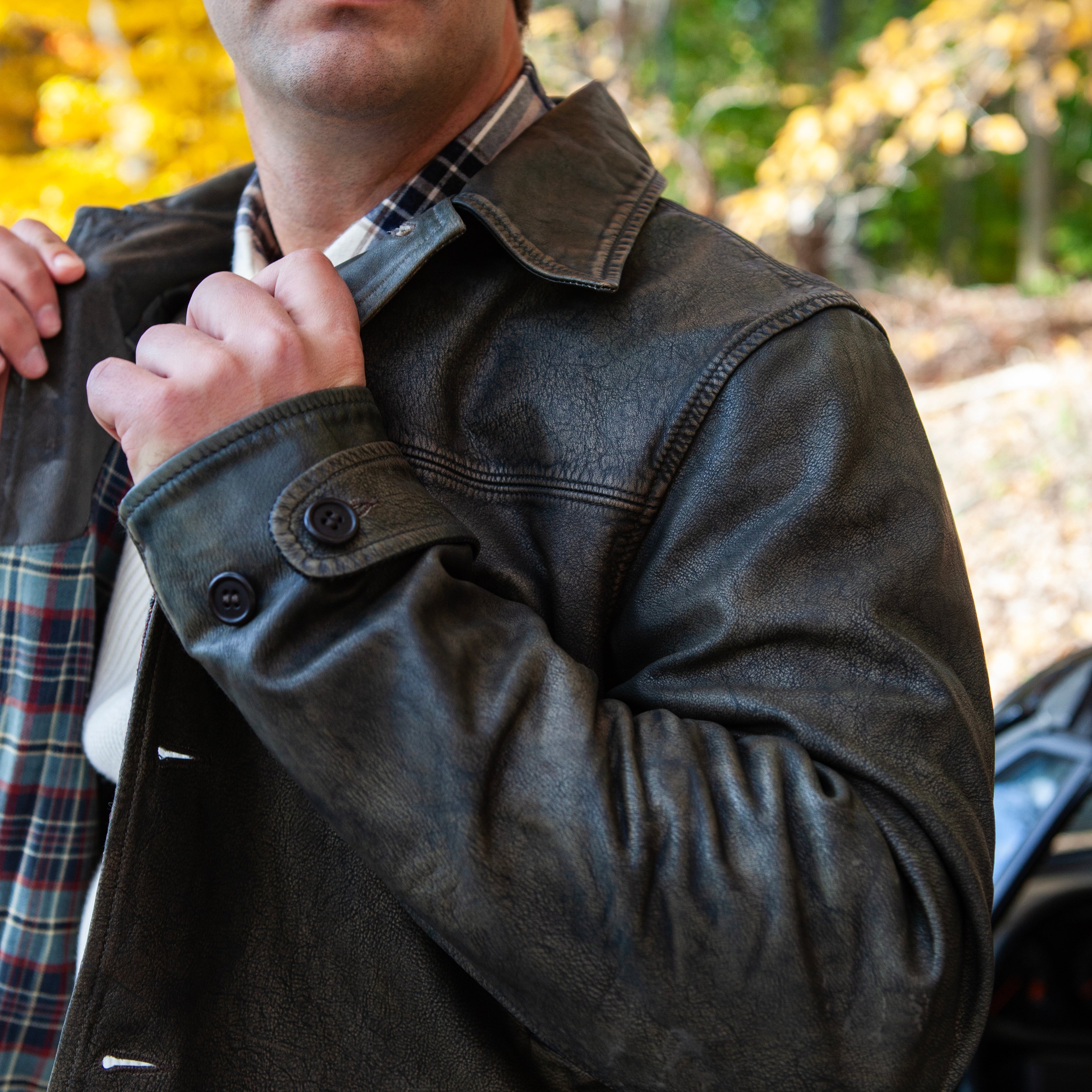 Man wearing sunglasses and a dark jacket with a blurred outdoor background