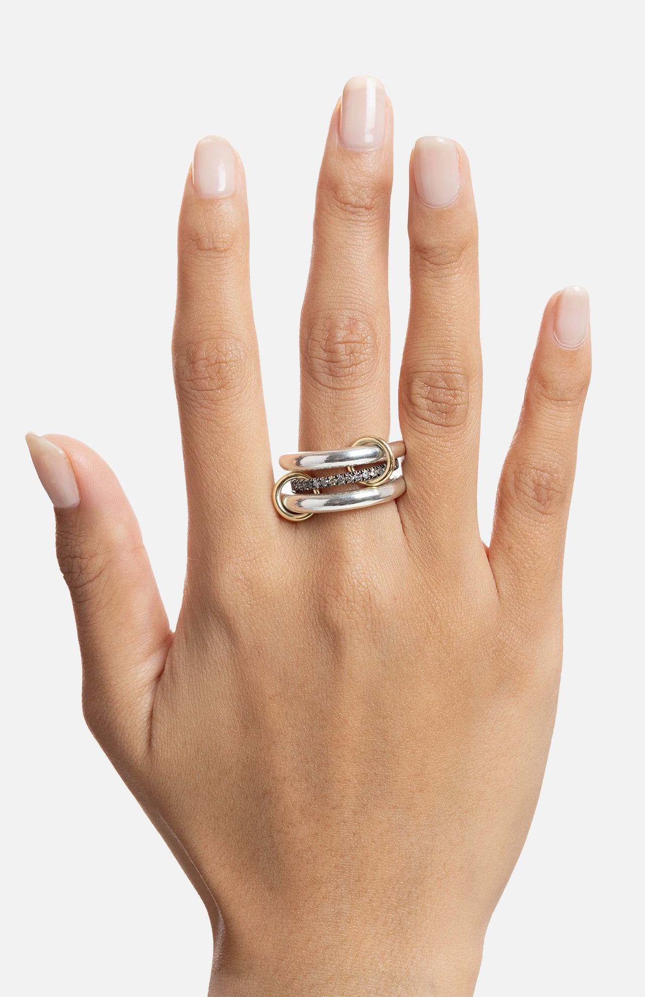 A hand with natural, neatly manicured nails wears the SPINELLI KILCOLLIN Libra Gris Diamond Ring—a chunky double-band design in sterling silver and gold with sparkling diamonds—on the middle finger against a white background.