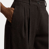 A person wearing the RALPH LAUREN COLLECTION Mini Herringbone Standard Pants with one hand in their pocket, showing the waistband, button, and part of a black shirt tucked in.