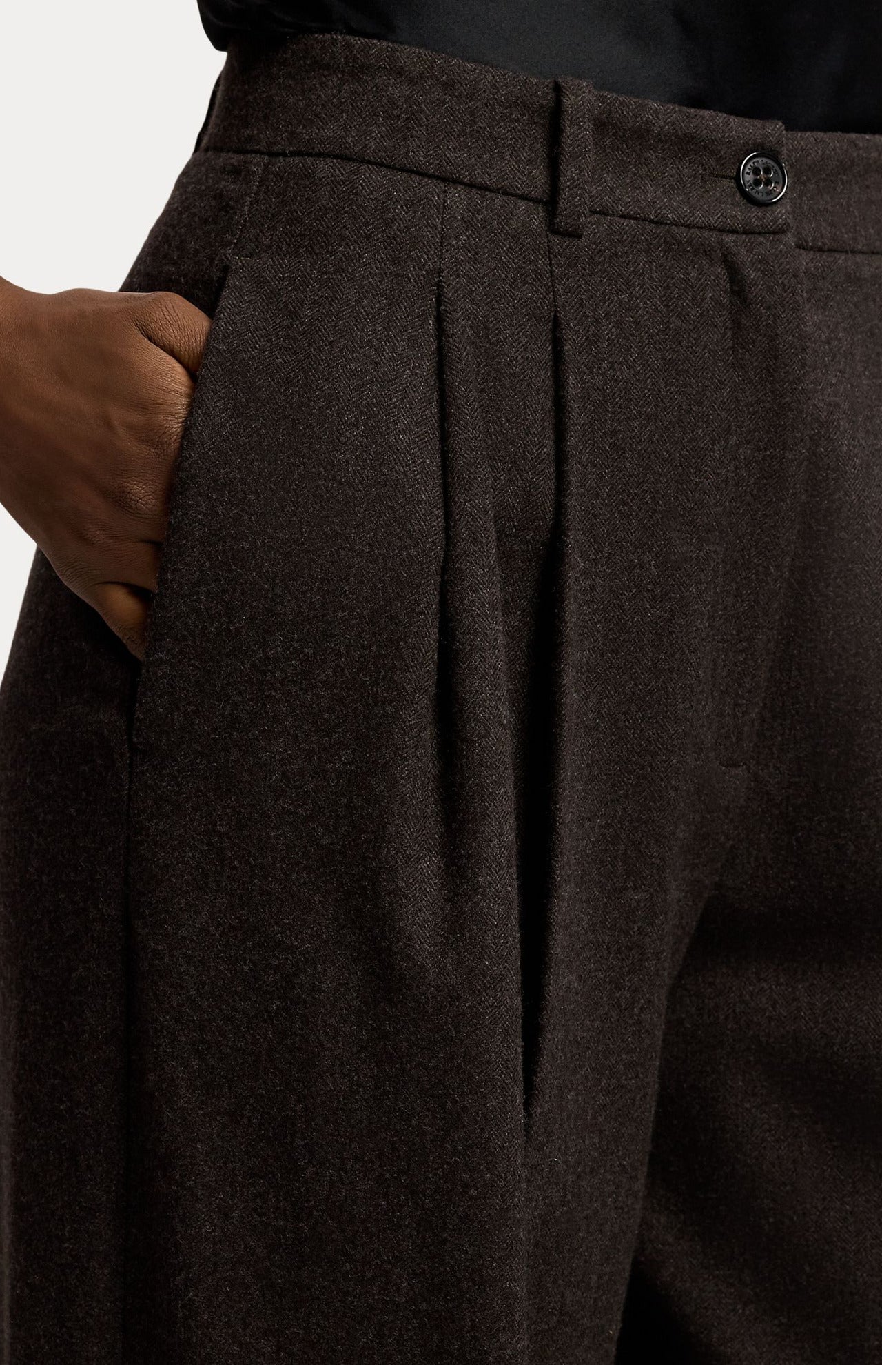 Close-up of dark brown Mini Herringbone Standard Pants in a relaxed fit, featuring front pleats and a side pocket.