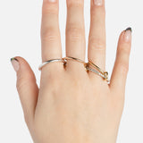 A hand with light skin and black-tipped French manicure nails wears the SPINELLI KILCOLLIN Nimbus 4 Band Diamond Ring along with two plain rings—one silver, one gold—against a white background.