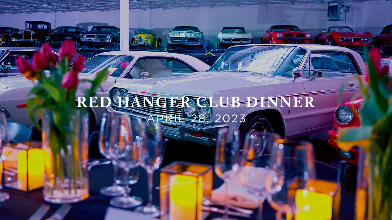 image with text "Red Hanger Club Dinner April 28, 2023" image is of a candlelit dinner table with a classic car garage in the background