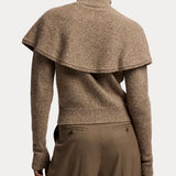 A person is shown from the back wearing a brown Cashmere Turtleneck Cardigan Sweater by RALPH LAUREN COLLECTION, styled with a cape overlay draped over the shoulders and paired with brown pants, evoking the elegance of fine Italian craftsmanship.