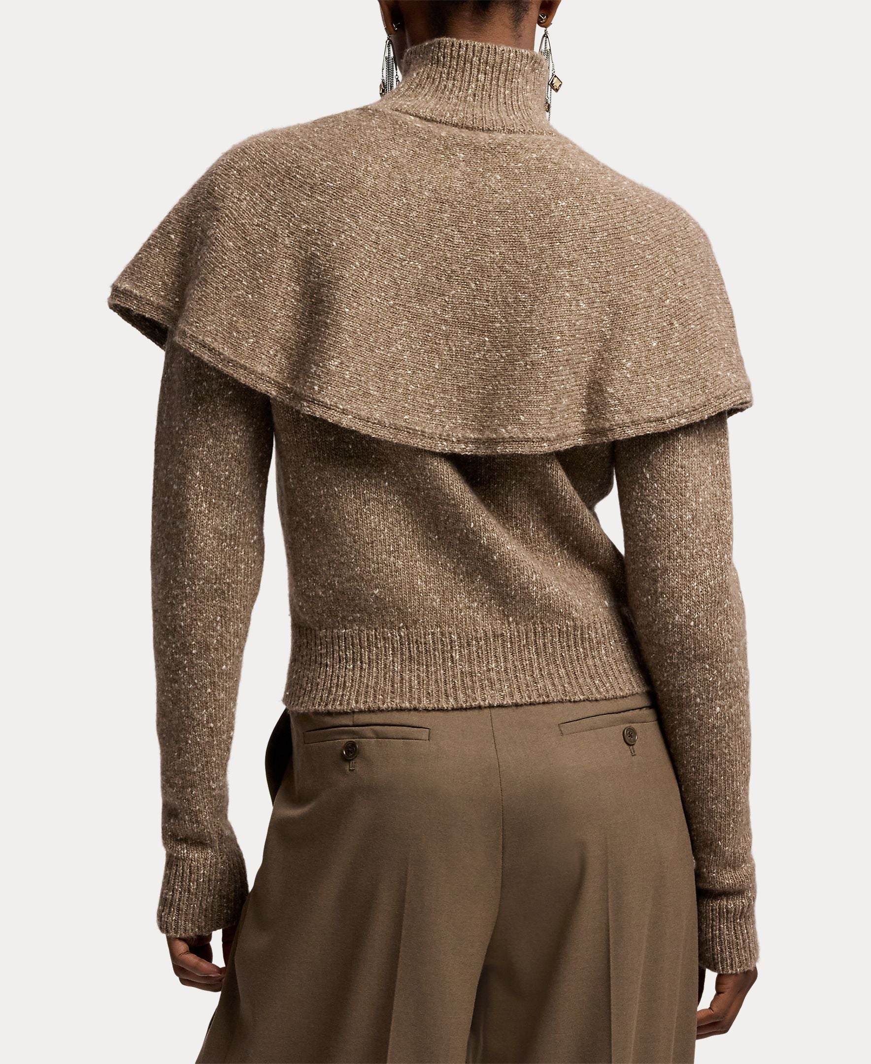 A person is shown from the back wearing a brown Cashmere Turtleneck Cardigan Sweater by RALPH LAUREN COLLECTION, styled with a cape overlay draped over the shoulders and paired with brown pants, evoking the elegance of fine Italian craftsmanship.