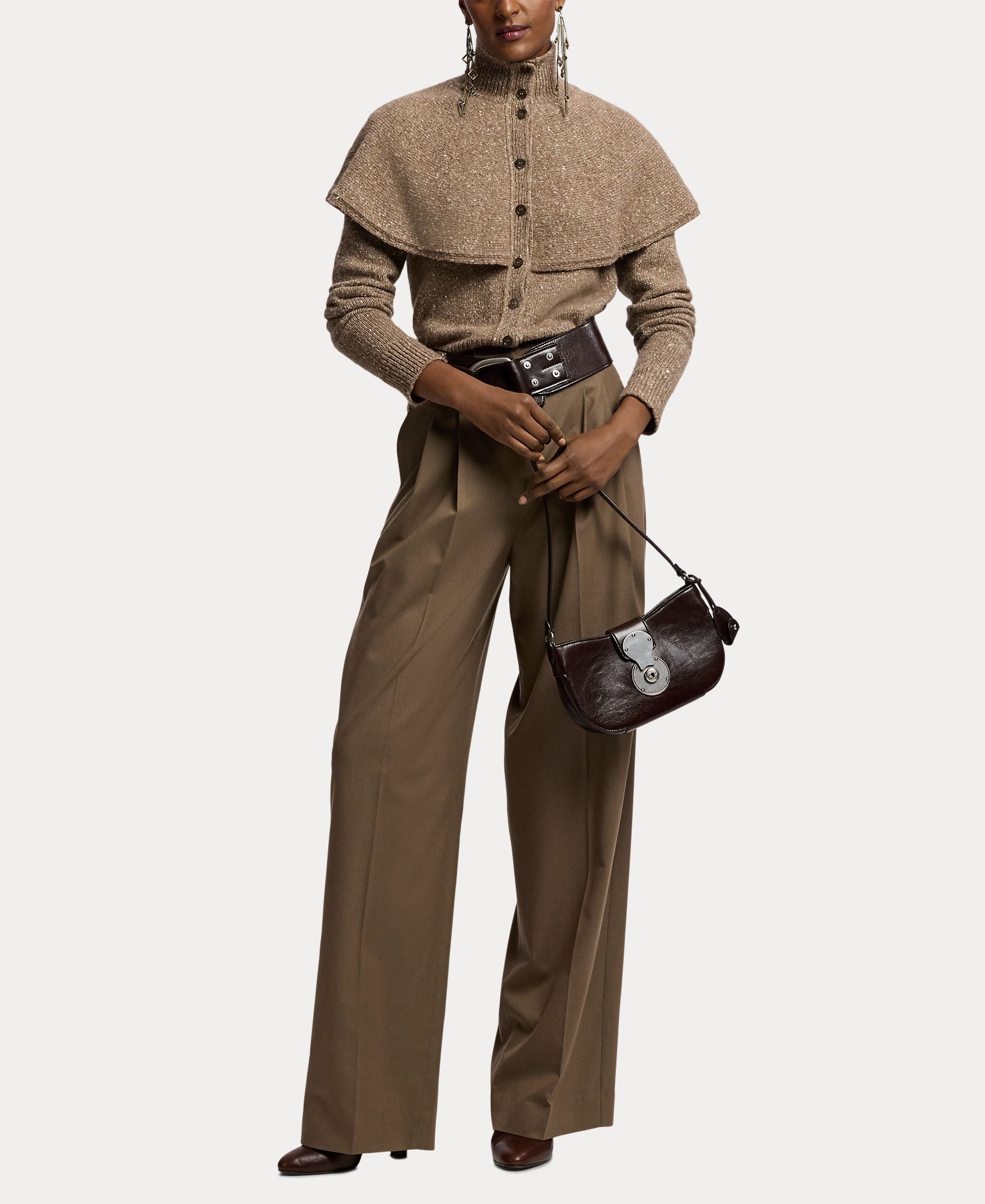 A person wearing the RALPH LAUREN COLLECTION Cashmere Turtleneck Cardigan Sweater layered over a collared shirt, paired with wide-leg brown trousers and heeled shoes, holds a dark brown purse while posing against a plain white background.