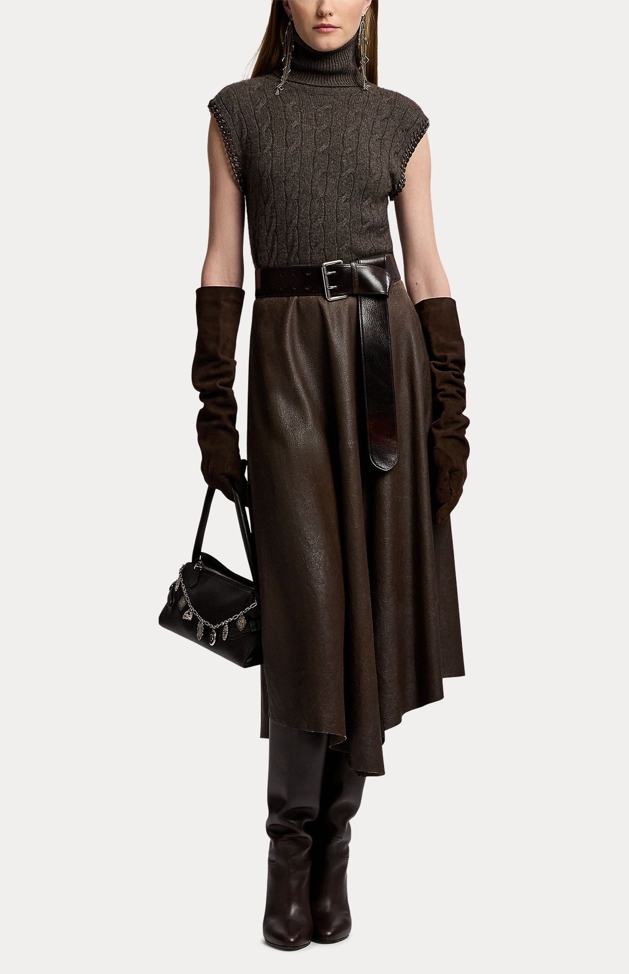 A person wearing a RALPH LAUREN COLLECTION Cashmere Turtleneck Sleeveless Sweater, a wide leather belt, a midi skirt, elbow-length gloves, and tall boots, while carrying a small handbag with chain detail.