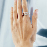A hand with manicured nails is shown against a metallic background, wearing the SPINELLI KILCOLLIN Solarium 3 Band Ring in sterling silver and yellow gold, one band featuring a delicate knot for added elegance.
