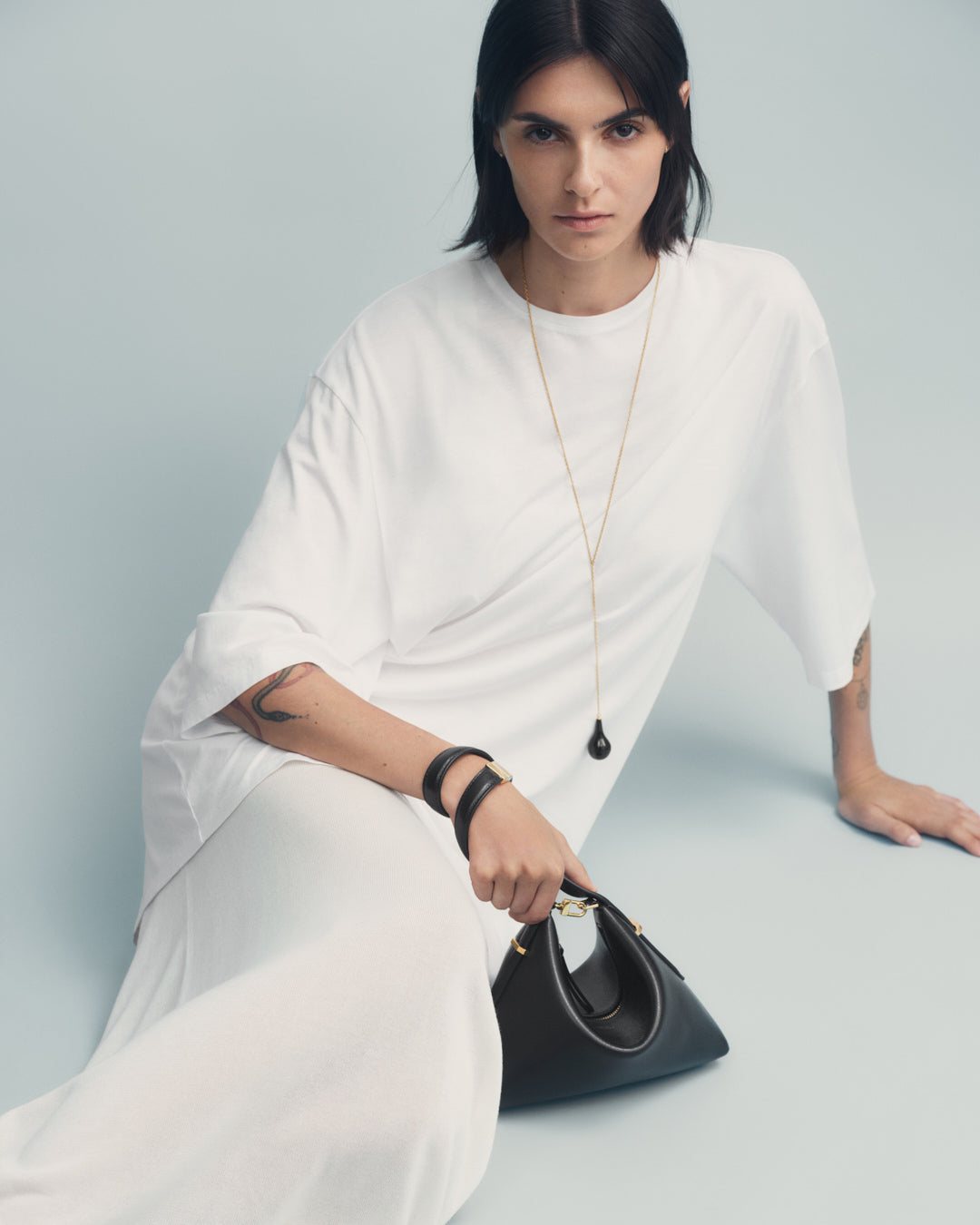 Woman in a white dress holding a black handbag against a light gray background