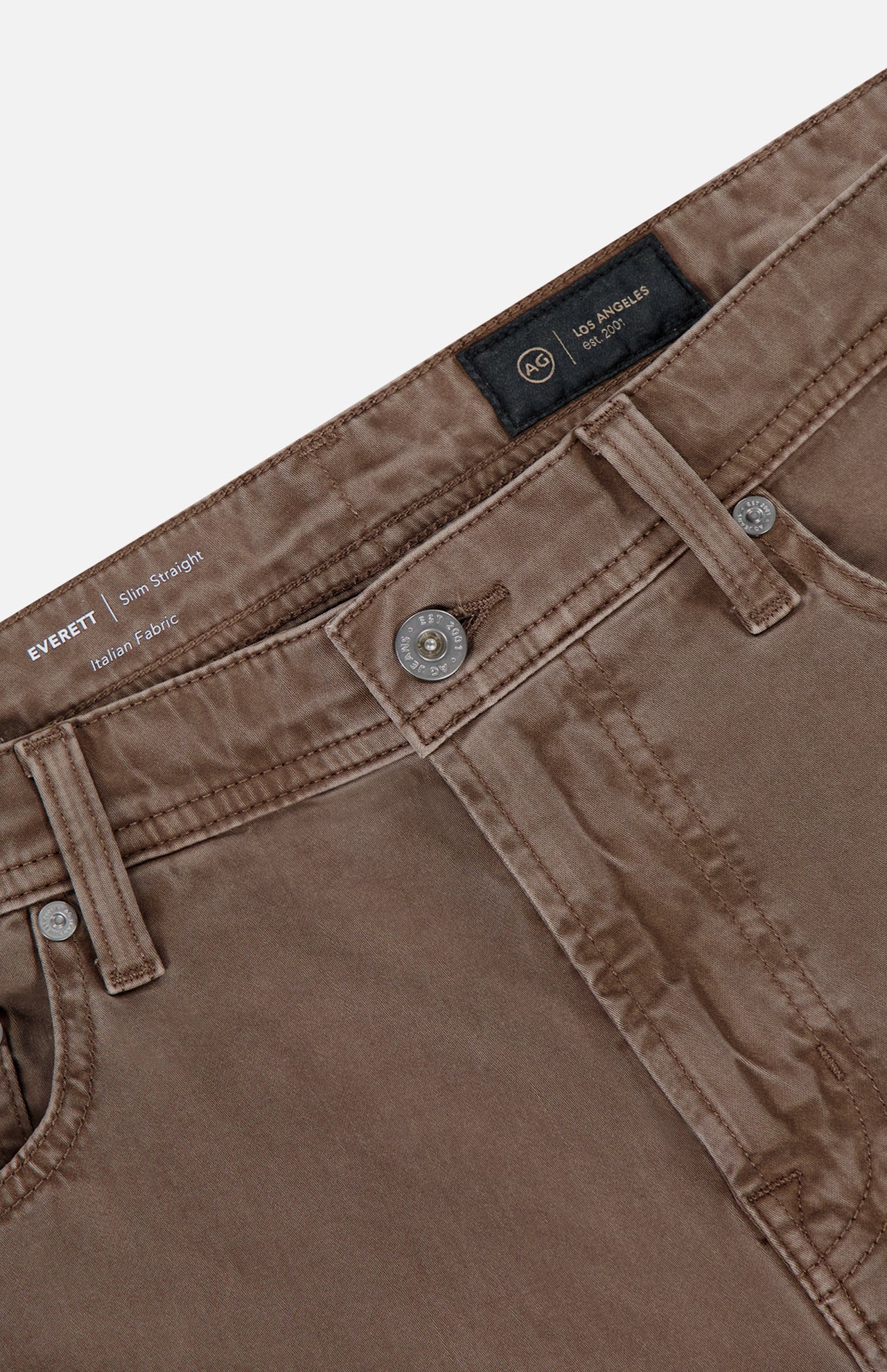 Close-up of Everett Slim Colored Jeans by AG in grey-brown, featuring waistband, button, belt loops, front pockets, and inner brand label. Made from Italian stretch sateen with a slightly worn finish for a casual look.