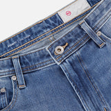Close-up of AG Everett All-direction Stretch Jeans in stretch denim, showing metal button, zipper, belt loops, and front pockets. A white label with red AG logo appears inside the waistband.