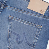 Close-up of the AG Everett All-direction Stretch Jeans' back pocket, showcasing visible stitching and a tan leather patch with AG embossed near the waistband, made from comfortable stretch denim.