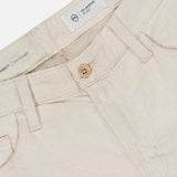 Close-up of the waistband and front of AG Everett Pants in light beige sustainable denim, featuring a wooden button, belt loops, front pockets, and an inner white label with AG branding and size details.