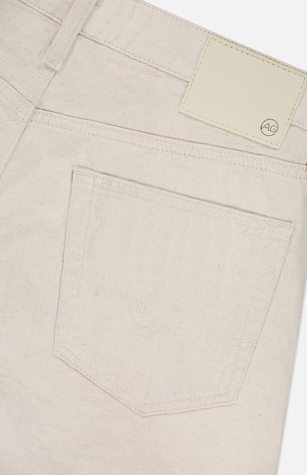Close-up of the back pocket on AG’s Everett Pants in cream-colored denim, slim straight fit, with a stitched pocket and a blank light leather patch featuring a small "AG" logo on the waistband.