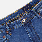 Close-up of the waistband and front pockets of AG's Cloud Soft Everett Jeans in Grove, featuring dark blue denim, slim fit, copper rivets, a metal button, visible stitching, and an interior label reading EVERETT and LOS GARZAS.