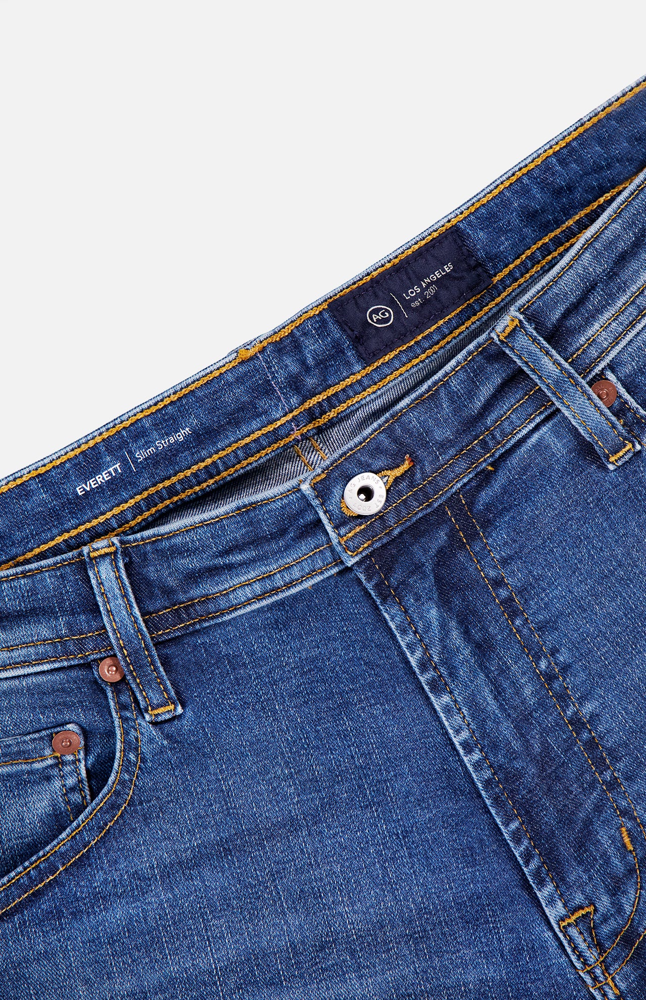 Close-up of the waistband and front pockets of AG's Cloud Soft Everett Jeans in Grove, featuring dark blue denim, slim fit, copper rivets, a metal button, visible stitching, and an interior label reading EVERETT and LOS GARZAS.