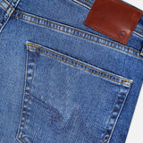 Close-up of the back pocket and waistband of AG’s Cloud Soft Everett Jeans in Grove, featuring slim fit dark blue denim with yellow stitching and a brown leather patch displaying the small AG logo.