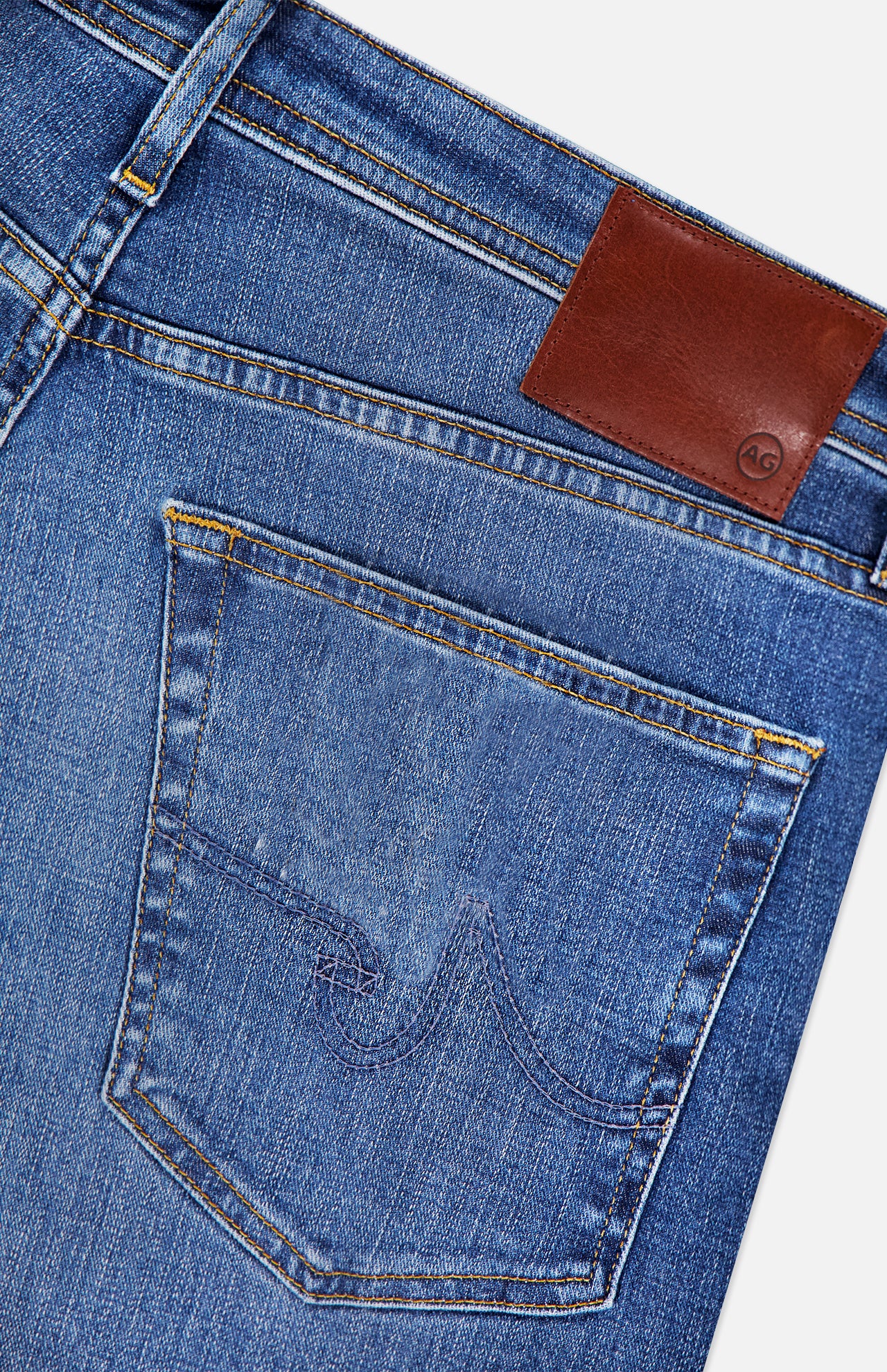 Close-up of the back pocket and waistband of AG’s Cloud Soft Everett Jeans in Grove, featuring slim fit dark blue denim with yellow stitching and a brown leather patch displaying the small AG logo.