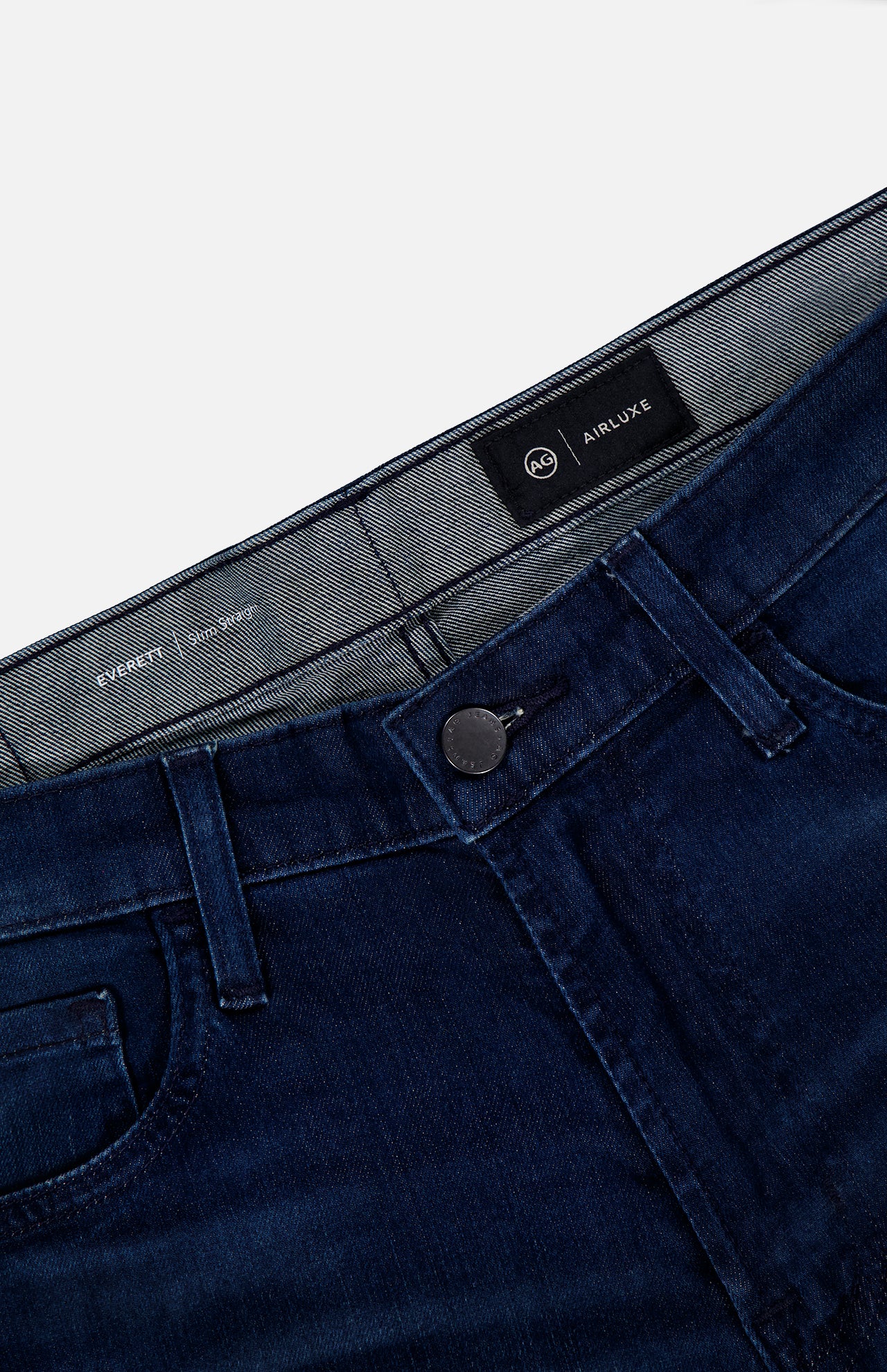 Everett Jeans in Yountville by AG shown laid flat on a white surface, featuring ultra-dark blue denim, slim straight fit, black button closure, front pockets, visible belt loops, and an Airluxe label inside the waistband.