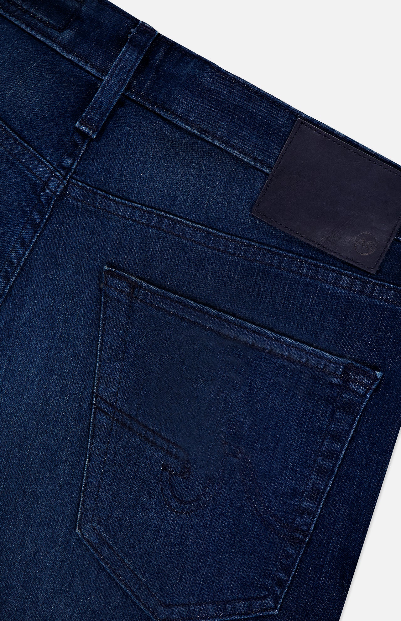 Close-up of the back pocket on AG Everett Jeans in Yountville: ultra-dark blue denim with detailed stitching, a belt loop, and a blank black leather patch on the waistband.