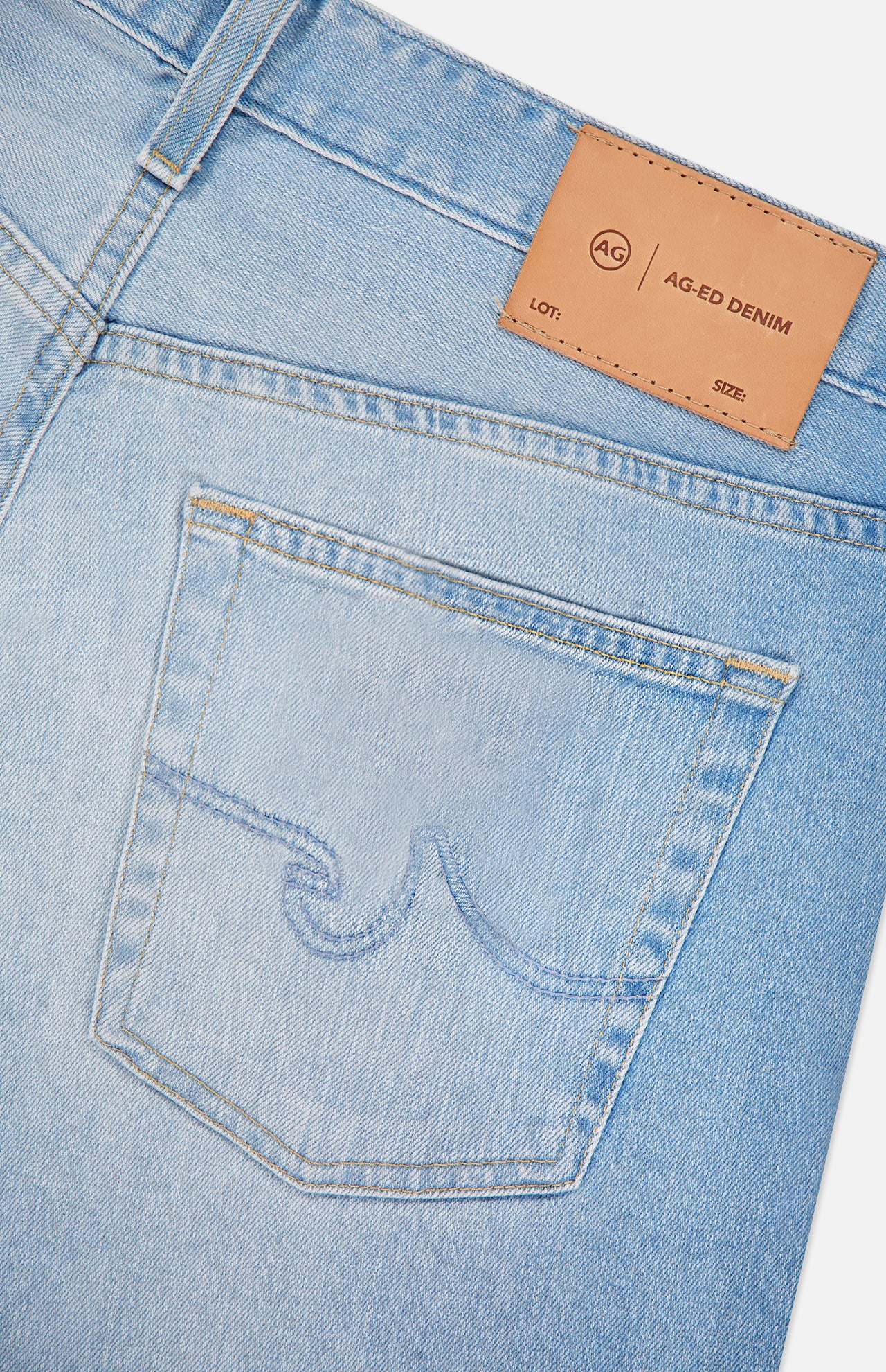 Close-up of AG's Everett Jeans in 22 Years: light blue wash slim fit style featuring a back pocket with stitched design, detailed seams, and a tan leather patch labeled “AG-ED DENIM” with lot and size fields.